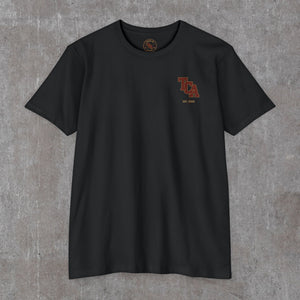 Front of the black Honor the Tradition tee with the small TCA monogram and EST. 2026 on the left chest