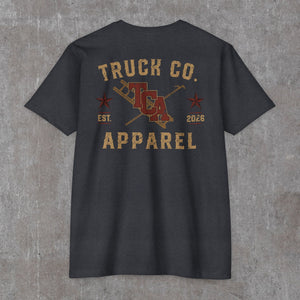 Back of the heather charcoal Truck Co. Apparel vintage logo tee: TCA crest between a crossed ladder and pike pole, two stars, EST. 2026