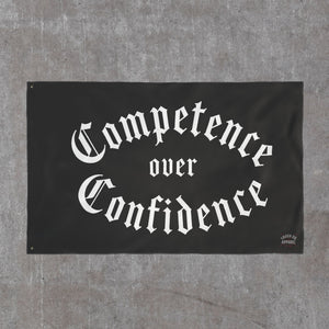 The larger 36 by 60 Competence over Confidence flag on a concrete wall, Truck Co. Apparel mark in the lower corner